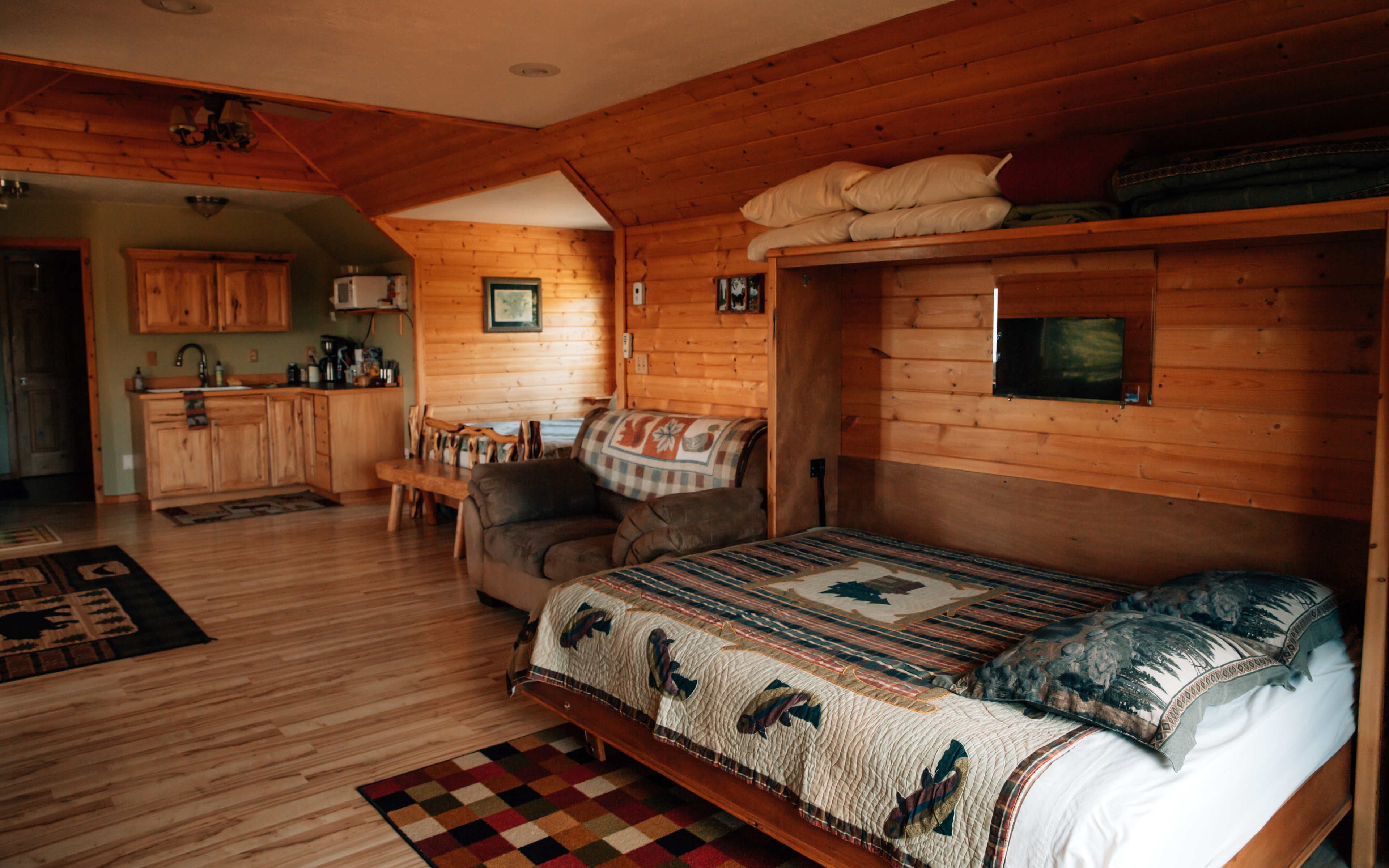 Bedroom with queen murphy bed, comfy upholstered chair, shelf with extra pillows & blankets