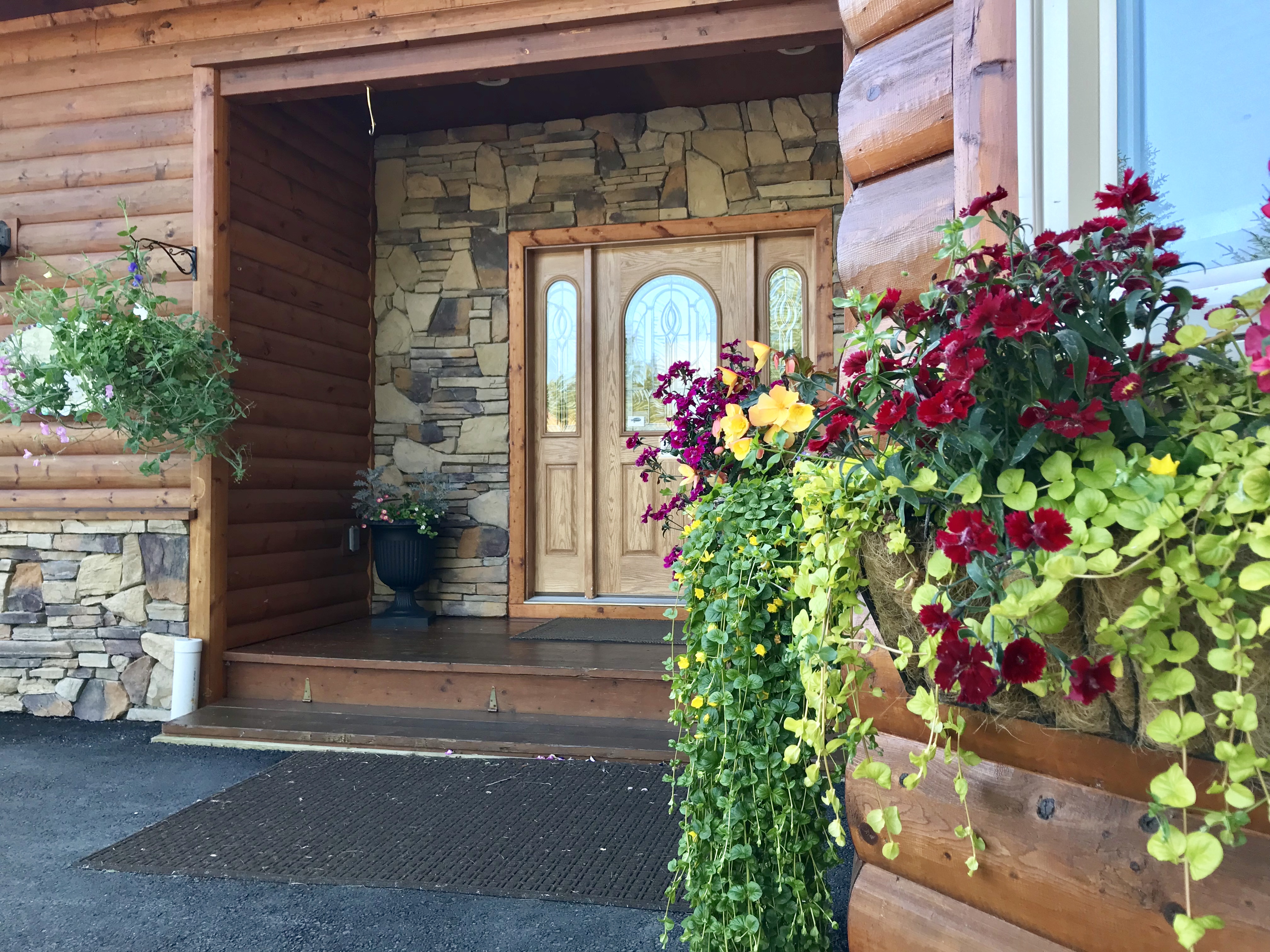 Entrance to The Main House featuring a beautiful wood door surrounded by stone, potted flowers and trailing vines