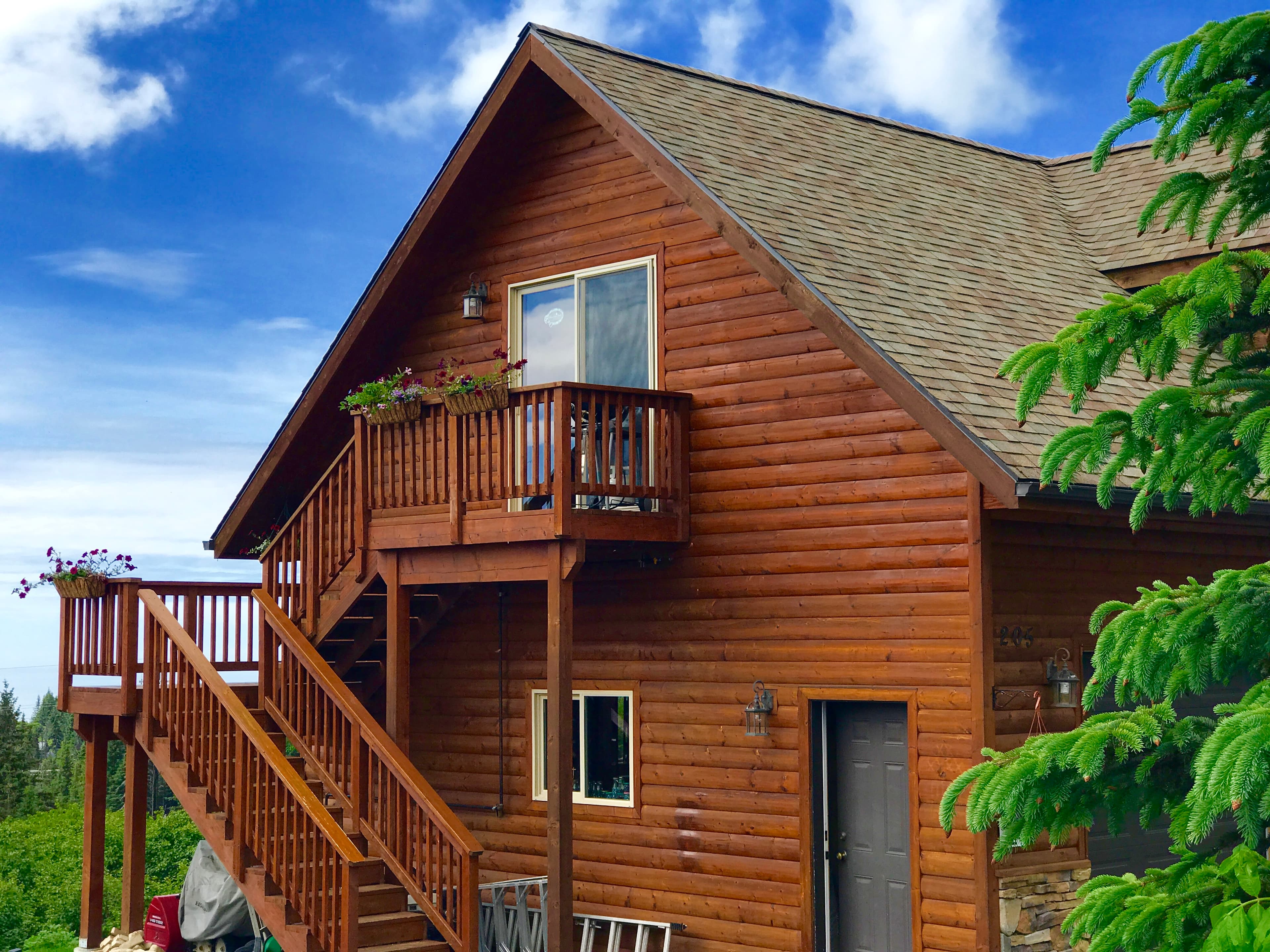 Exterior of two story log home with exterior stairs, trees, and bright blue sky